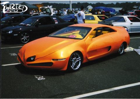 1990 Ford Bronco - A custom orange sports car with a unique body style is parked at an outdoor event.