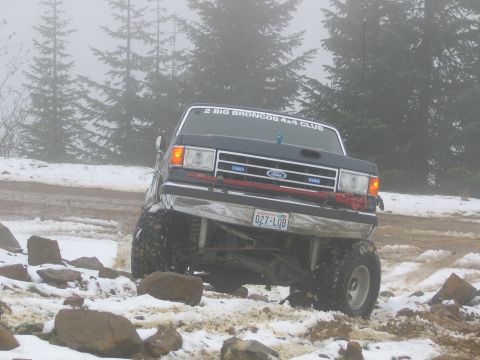 1991 Ford Bronco - Modified Ford Bronco navigating a snowy trail with trees in the background.