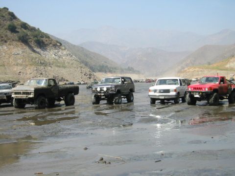 1985 Ford Bronco - A group of off-road vehicles gathered in a scenic, muddy terrain.
