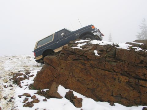 1991 Ford Bronco - A 1991 Ford Bronco navigates a rocky, snow-covered incline on a foggy day.