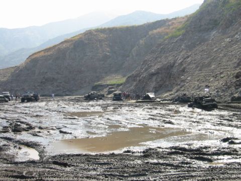 1985 Ford Bronco - Multiple off-road vehicles navigate a challenging muddy terrain with steep hills.