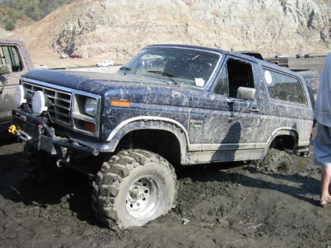 1985 Ford Bronco - A muddy blue Ford Bronco is stuck in a muddy area with a rocky hillside in the background.