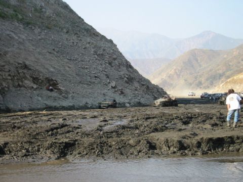 1985 Ford Bronco - Several off-road vehicles are stuck in a muddy, mountainous landscape, with a person observing the scene.