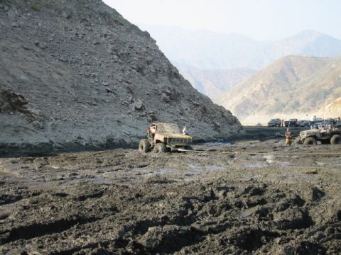 1985 Ford Bronco - Off-road vehicles navigate a challenging muddy terrain with mountainous scenery.