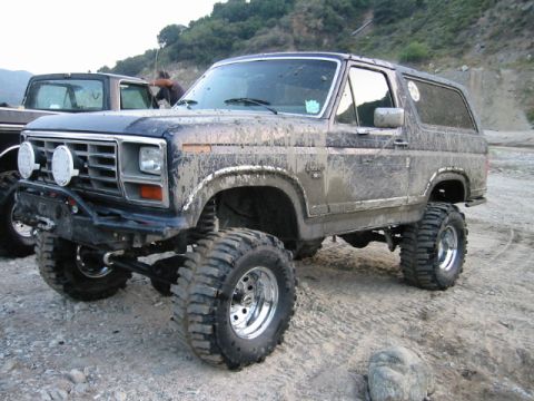 1985 Ford Bronco - This lifted SUV is covered in mud, suggesting it has been off-roading.