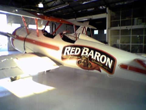 1998 Ford Crown Victoria - A biplane with a 'Red Baron Quality' logo is parked inside a hangar.