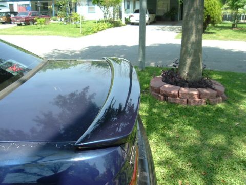 1993 Ford Taurus - Rear view of a dark blue sedan with a spoiler, parked in a residential area with other vehicles visible.