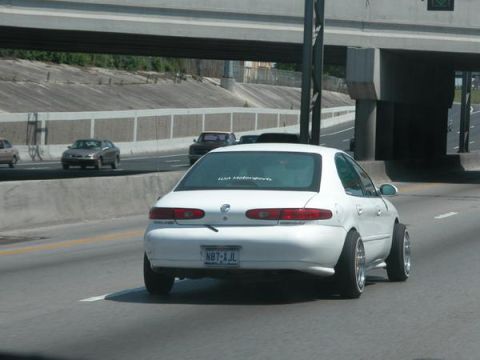 1993 Ford Taurus - White sedan with aftermarket wheels on the highway. The album claims it's a 1993 Ford Taurus.