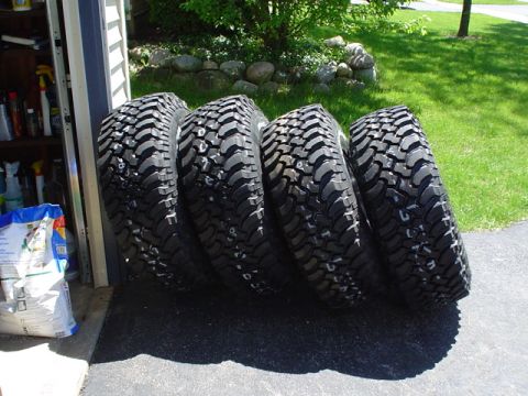 1993 Ford Bronco - A set of four large off-road tires are shown leaning against a garage door, ready for installation.