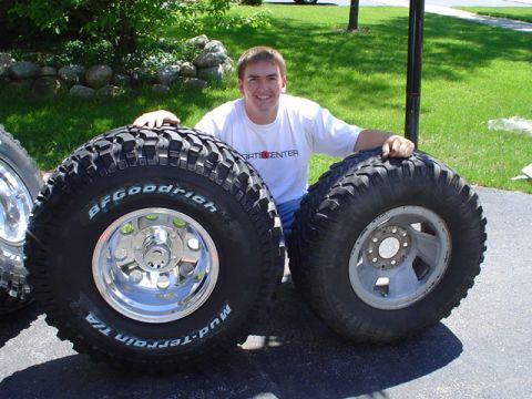 1993 Ford Bronco - A man proudly displays two oversized off-road tires, each mounted on a different style of rim.