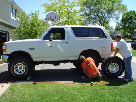 1993 Ford Bronco - Two people are working on a white 1993 Ford Bronco with large tires in a driveway.