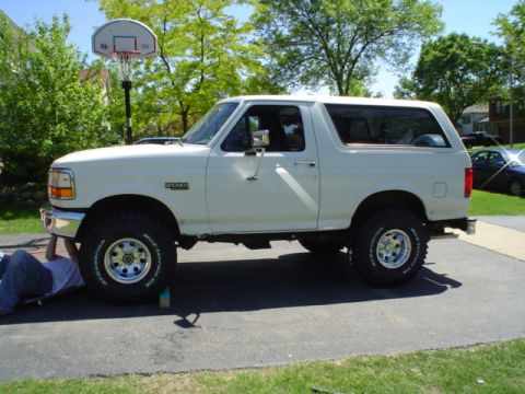 1993 Ford Bronco - A person works on a lifted white Ford Bronco parked in a driveway with a basketball hoop in the background.