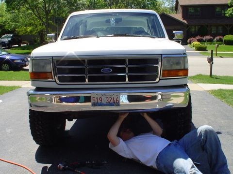 1993 Ford Bronco - A man works on the underside of a white Ford truck parked in a driveway.