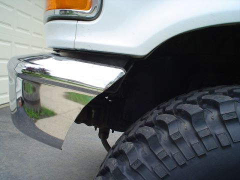 1993 Ford Bronco - Close-up of a white SUV's front corner, showing a chrome bumper and a large, off-road tire.