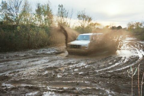 1993 Ford Bronco - A 1993 Ford Bronco navigates a challenging muddy terrain, creating a large splash.