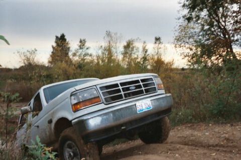1993 Ford Bronco - This silver pickup truck navigates a dirt path, its grille clearly visible.