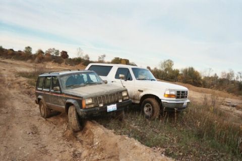 1993 Ford Bronco - Two SUVs parked on a dirt road with grassy hills in the background.