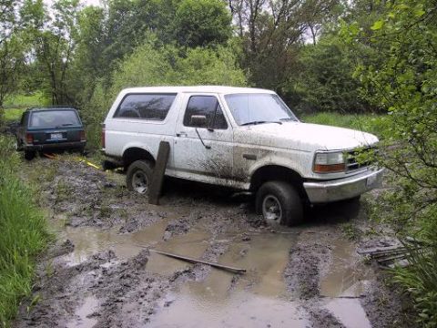 1993 Ford Bronco - A white 1993 Ford Bronco is stuck in a muddy trail, with another vehicle attempting to pull it out.