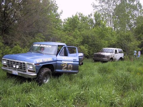1993 Ford Bronco - Two off-road vehicles are parked in a grassy area with trees in the background.