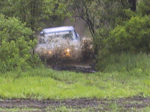 Off-road vehicle driving through a muddy puddle, splashing water. Text on vehicle reads 'ZURICH'