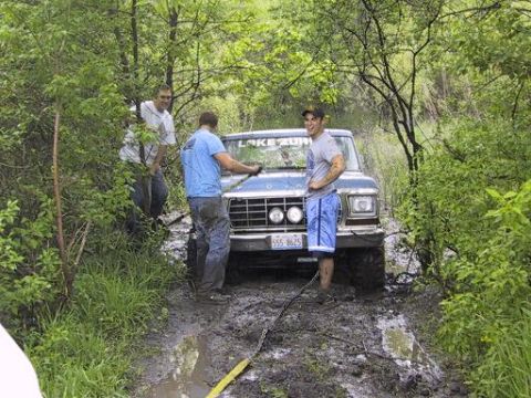 1993 Ford Bronco - Three men are gathered around a blue Ford Bronco that is stuck in a muddy, wooded area.