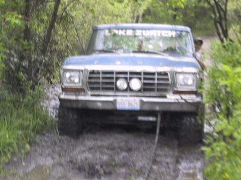 1993 Ford Bronco - This blue Ford truck, likely from the late 1970s, is struggling through a muddy, wooded path.