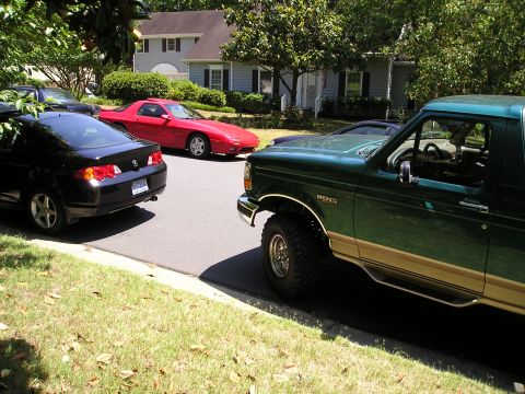 1996 Ford Bronco - A lifted green Ford Bronco is parked on the street in front of a house, with other cars nearby.