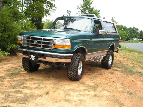 1996 Ford Bronco - This lifted 1996 Ford Bronco is shown from a three-quarter front angle, parked outdoors on a dirt surface.
