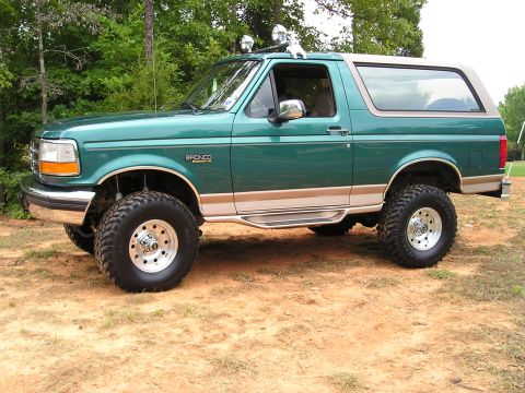 1996 Ford Bronco - Lifted 1996 Ford Bronco in green with tan two-tone trim sits on dirt.