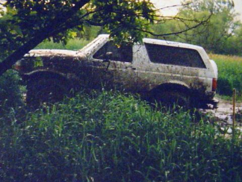 1993 Ford Bronco - Mud-covered 1993 Ford Bronco stuck in a grassy, muddy field.