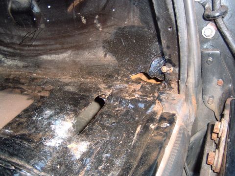 1993 Ford Bronco - The interior floor of a vehicle shows signs of rust and dirt, with a visible hole and some webbing.