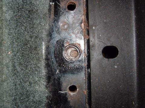 1993 Ford Bronco - Detail of a metal bracket with visible bolt holes and a bolt head, likely a vehicle component.