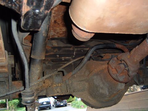 1993 Ford Bronco - Underside view of rusty rear axle and suspension components, with two cars in the background.