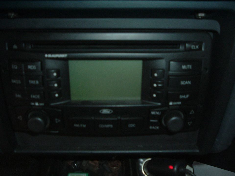Car stereo with a green display and various buttons, including 'MUTE', 'SCAN', and 'MENU'