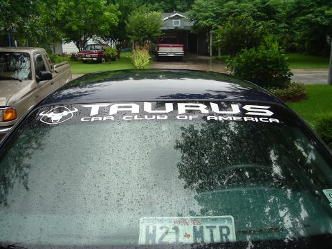 1993 Ford Taurus - A dark sedan displays a club sticker on its rear window, with other vehicles visible in the background.