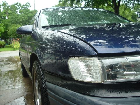 1993 Ford Taurus - Front passenger side view of a dark blue 1993 Ford Taurus on a rainy day.