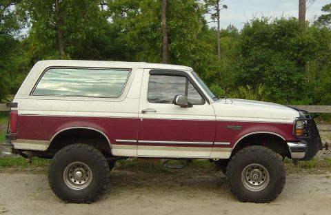 1993 Ford Bronco - Side view of a lifted 1993 Ford Bronco with two-tone paint and off-road tires.