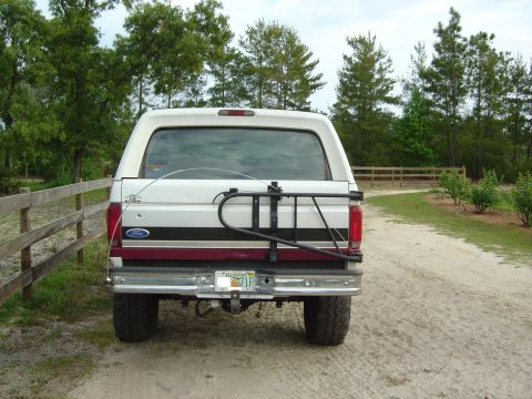 1993 Ford Bronco - The rear of a 1993 Ford Bronco is shown parked on a dirt road next to a wooden fence.