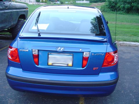 1979 Ford Bronco - Rear view of a bright blue Hyundai Elantra GT hatchback parked on asphalt beside a grass lawn, showing the tailgate badging, blanked-out li…