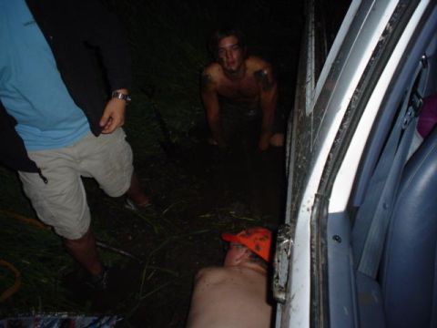 1993 Ford Bronco - Several people are in a muddy area next to a vehicle, appearing to be stuck or recovering from an off-road incident.