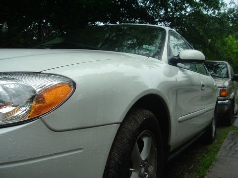 2003 Ford Taurus - A white 2003 Ford Taurus is parked outside, with another vehicle visible behind it.