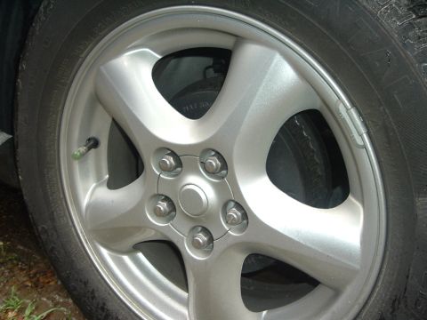 2003 Ford Taurus - A close-up view of a silver alloy wheel, showing the lug nuts and tire tread.