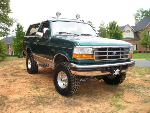 1996 Ford Bronco - This lifted 1996 Ford Bronco is shown from a 3/4 front angle, parked on dirt with a house in the background.