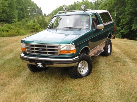 1996 Ford Bronco - This lifted Ford Bronco is parked on a grassy incline with trees and power lines visible in the background.