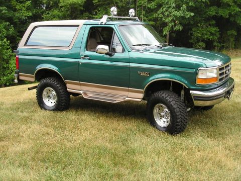 1996 Ford Bronco - A lifted green 1996 Ford Bronco with tan accents and a roof rack sits on a grassy lawn.