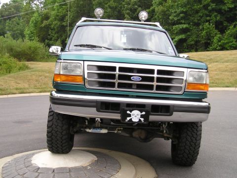 1996 Ford Bronco - This lifted green Ford Bronco is shown from the front, a custom license plate frame and auxiliary lights on the roof rack.