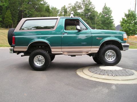 1996 Ford Bronco - A lifted green Ford Bronco with tan trim is parked on a circular stone feature.