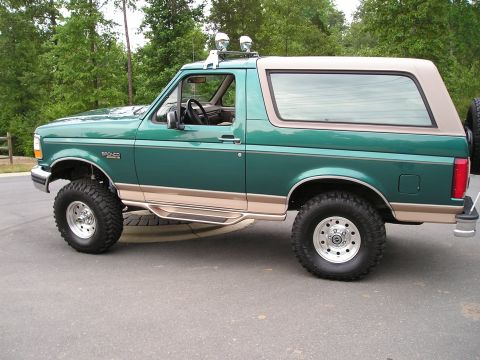1996 Ford Bronco - Side view of a lifted 1996 Ford Bronco with two-tone paint and off-road tires.