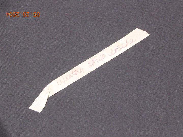 Strip of white tape on dark fabric hand-labeled in pen 'weather strip inside', dated 2004