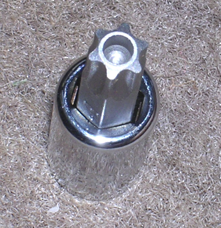 Chrome lug-style bolt or stud with star-shaped hole sitting in tan carpet, close-up